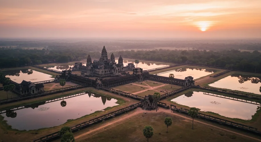 Aerial view of Angkor Wat temple complex at sunrise, with moats reflecting the pink and orange hues 