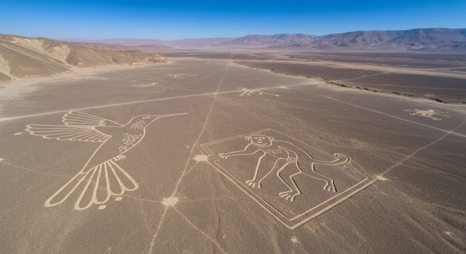 A sweeping aerial view of the Nazca Desert in Peru, showcasing several massive geoglyphs including a