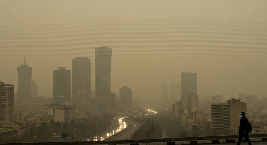A panoramic view of Tehran shrouded in a thick, yellowish-brown smog. Tall buildings are barely visi