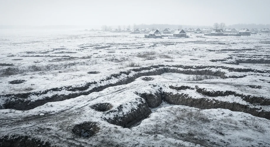 A panoramic view of a Ukrainian landscape in winter. The land is scarred by trenches and bomb crater