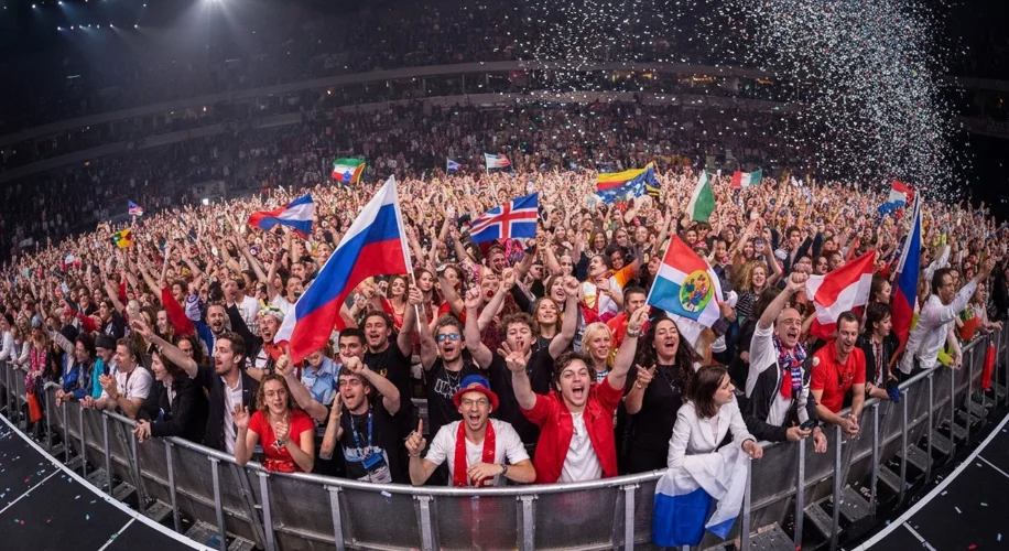 A diverse crowd of people from different European countries cheering and waving flags at a Eurovisio