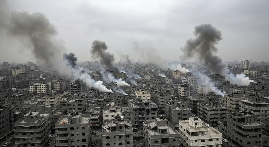 An aerial view of Gaza City, showing dense urban neighborhoods with smoke rising from distant explos